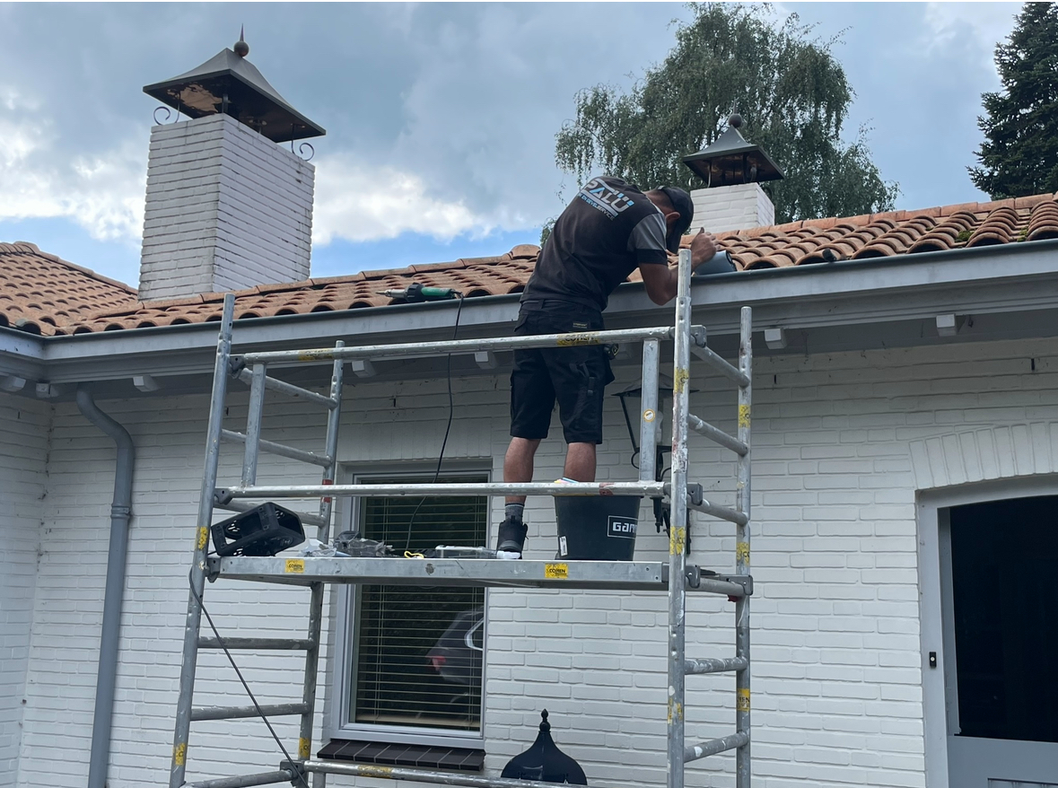 Dakgoot en dakrand herstellen in Enschede Dakdekker herstelt de dakgoot en dakrand van een pannendak bij een woning in Enschede.