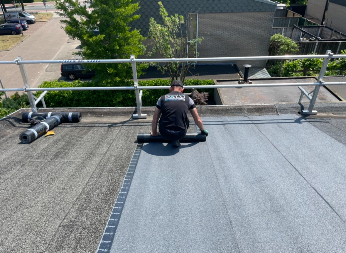 Dakdekker rolt nieuwe bitumen dakbedekking uit op een plat dak in Enschede.